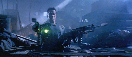 Arnold firing two large guns, one in each hand, followed by bad guys flying across a large industrial space. Animated GIF activated on mouseover.