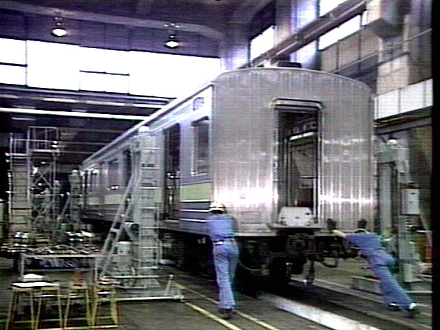 Video screen shot of workers moving a subway car in a maintenance shop